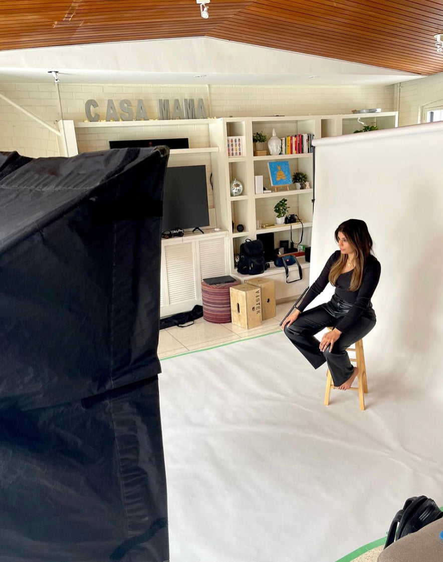Amrit Singh sitting on a stool in a room with a white backdrop, black furniture, and a 'Casa Nana' sign.