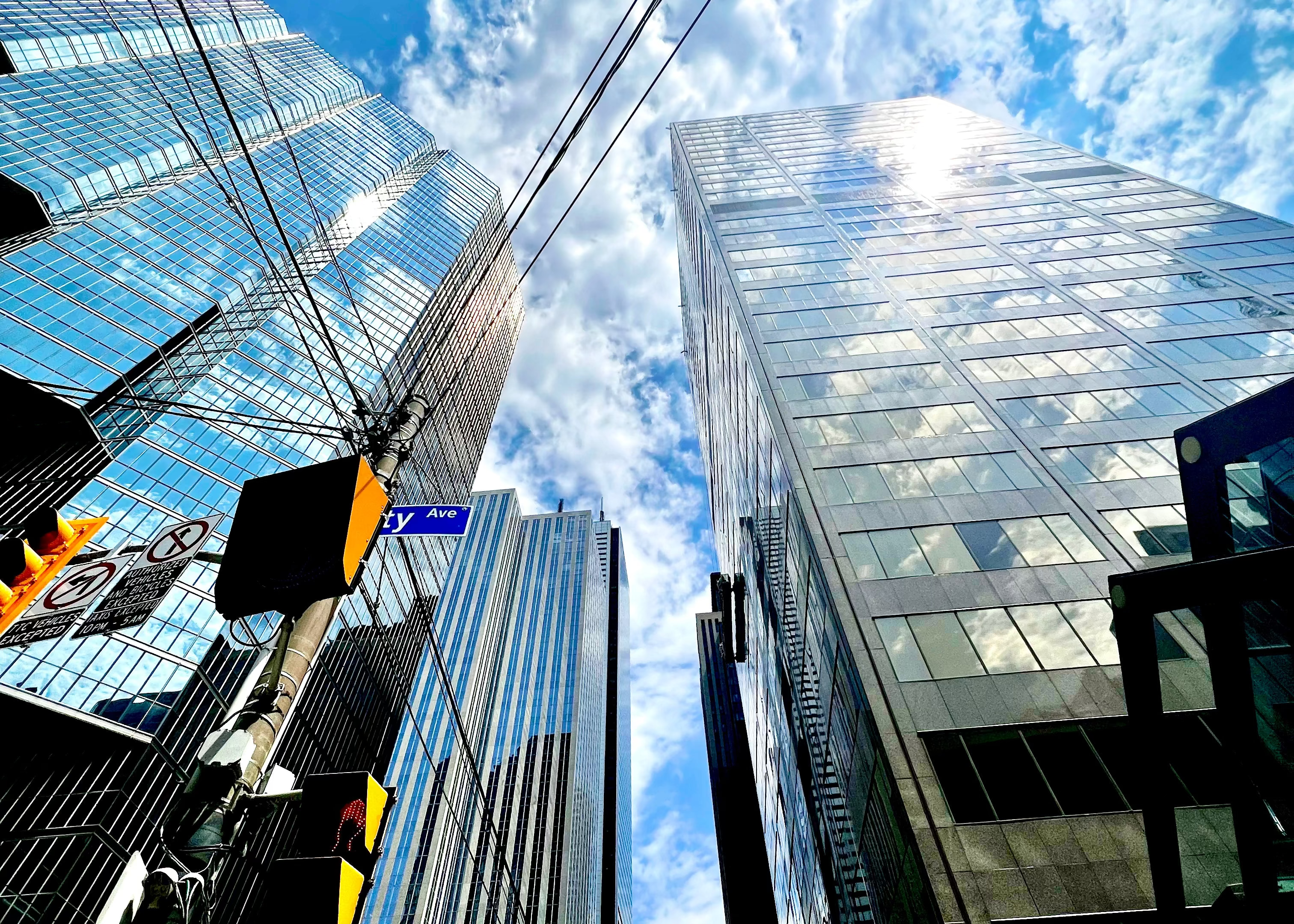 Tall glass buildings with a clear blue sky and white clouds.