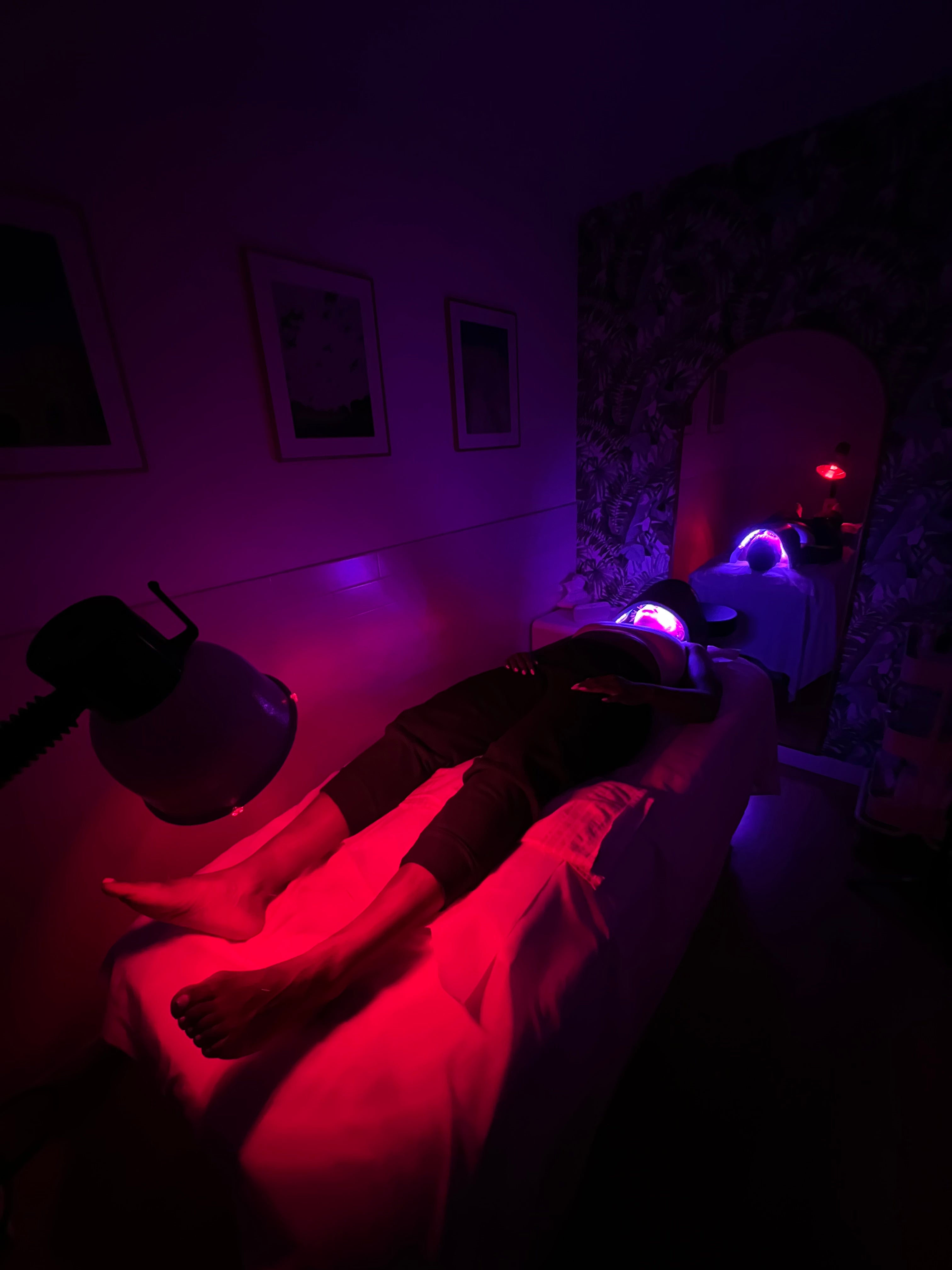 Person lying on a bed in a dimly lit room with red and purple lighting.