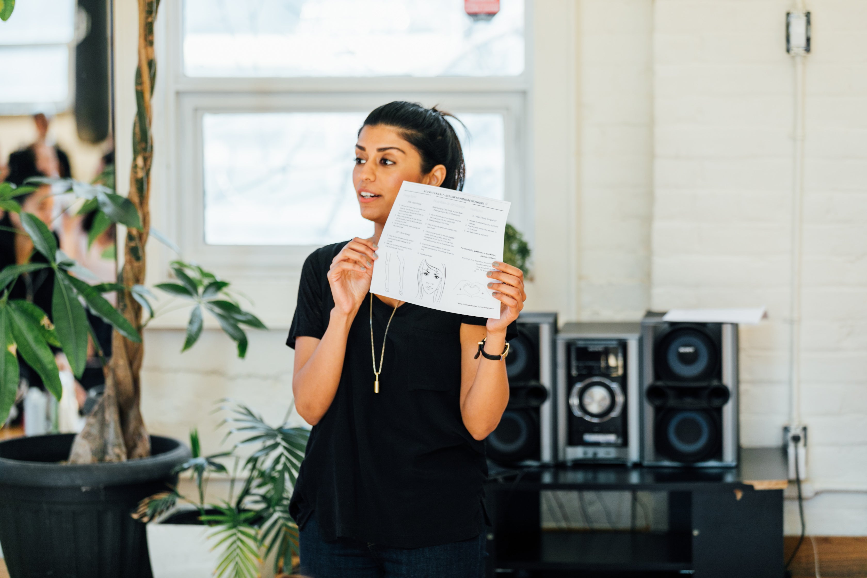 Women teaching a class and holding an acupuncture paper with both hands.
