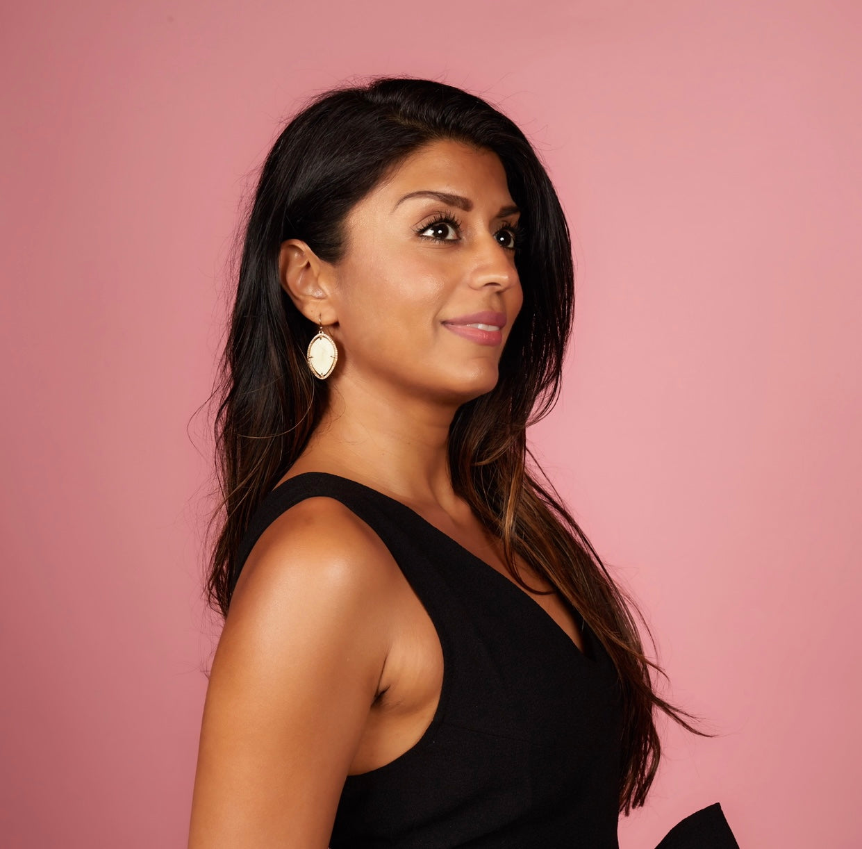 Amrit Singh wearing a black dress with long earrings against a pink background